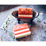 Striped red and white bar soaps, one in a small metal bathtub dish on a textured surface.