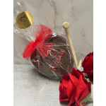 Wrapped chocolate heart with red bow and wooden mallet beside two red roses.