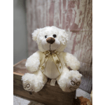 White teddy bear with a gold ribbon sitting on a wooden surface