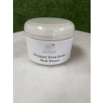 A white jar labeled whipped shea butter sits on a table.