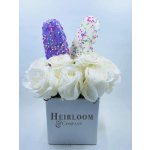 White roses in a square vase with two sprinkle-covered treats