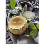 A jar candle with a decorative lid on gray fabric, accented by green leaves.
