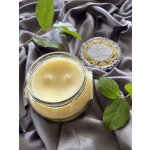 Glass jar candle with a decorative lid on draped fabric and green sprigs