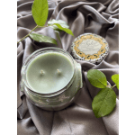 A glass jar candle with a matching lid on draped fabric, accented by green leaves