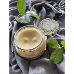 Beige candle in a glass jar with a decorative lid and green leaves