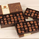 Three boxes of assorted chocolates on a light wooden surface