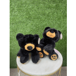 Two black teddy bears with orange paws sit on a round white table.