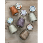 Assorted scented candles in textured glass jars with colorful wax and decorative lids on a wood surface