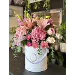 Pink lilies, hydrangeas, roses, and carnations arranged in a round white hatbox.