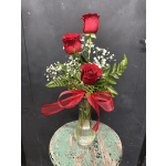 Three red roses in a glass vase with baby's breath and a red ribbon