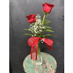 Two red roses in a glass vase with baby's breath and a red ribbon