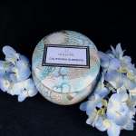 Round Voluspa candle tin surrounded by pale blue flowers
