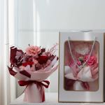 Bouquet of pink and red roses in pink wrapping beside a gift bag