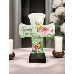 Memorial cross with butterflies and pink flowers on a table beside candles