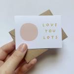 Hand holding a small greeting card that says "LOVE YOU LOTS"