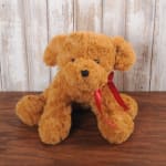 Brown plush puppy with a red satin ribbon sitting on a wooden surface