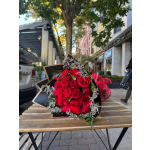 Bouquet of red roses with white filler flowers wrapped in black paper on a wooden outdoor table