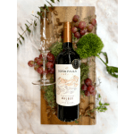 Bottle of red wine with empty wine glass, grapes, and moss on a wooden board