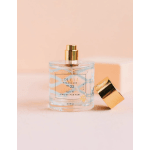 Perfume bottle with a gold cap and matching lid on a pink background