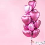 Cluster of pink heart-shaped balloons held against a pink background