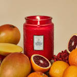Red jar candle surrounded by assorted fruit