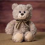 Plush teddy bear with a plaid bow sitting on a brown surface
