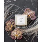 White candle in a glass tumbler surrounded by spotted orchid blooms