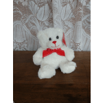 White teddy bear with a red bow sitting on a wooden surface