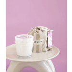 White candle in a glass jar beside a striped fabric pouch on a stool