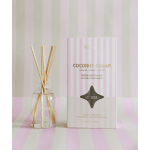 Reed diffuser in a clear glass bottle beside a striped pink box