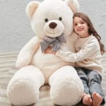 Girl hugging a large white teddy bear with a checkered bow