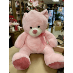 Large pink teddy bear with a ribbon sitting in a flower shop