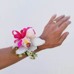 White orchid wrist corsage with a pink ribbon on a hand