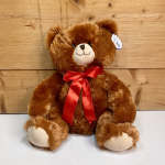 Brown teddy bear with a red ribbon bow sitting against a wood backdrop