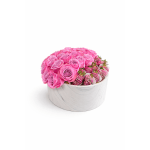 Round white box filled with pink roses and chocolate-covered strawberries drizzled with pink and white.