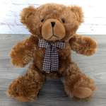 Brown teddy bear with a plaid bow tie sitting on a wooden surface