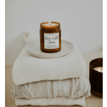 Lit amber candle in a glass jar on folded white blankets