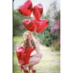 Woman in a red dress holding red heart-shaped balloons outdoors