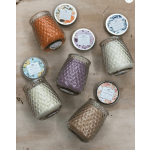 Assorted colored jar candles with patterned lids arranged on a light wood surface