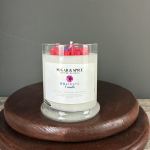 White scented candle in a clear glass jar with red wax accents on a wooden stand