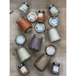Assorted colored candles in textured glass jars with decorative lids arranged on a wooden surface