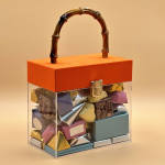 Clear gift box with assorted chocolates and an orange lid with handle