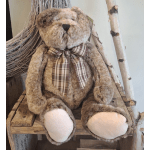 Plush teddy bear with a plaid bow sitting on a wooden shelf