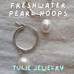 Silver hoop earrings with dangling pearls on a textured fabric background