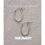 Pair of silver oval hoop earrings on a textured fabric background