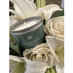 White roses and lilies arranged around a green candle tin