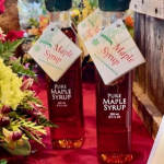 Two bottles of maple syrup with hanging tags beside flowers
