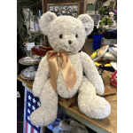 Large cream teddy bear with a satin bow sitting in a shop display