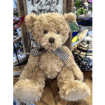 A plush teddy bear with a checkered bow sits on a store shelf.