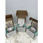 Three boxed candles with floral labels arranged on a table.